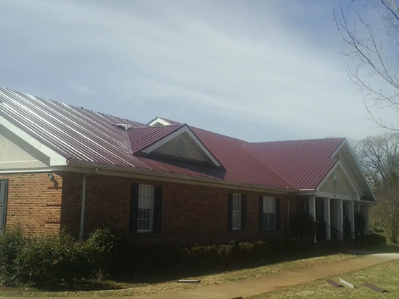 Red metal roof with gabled entries on a long brick building, from a Hail Damage Roof Repair job in Washingtonville