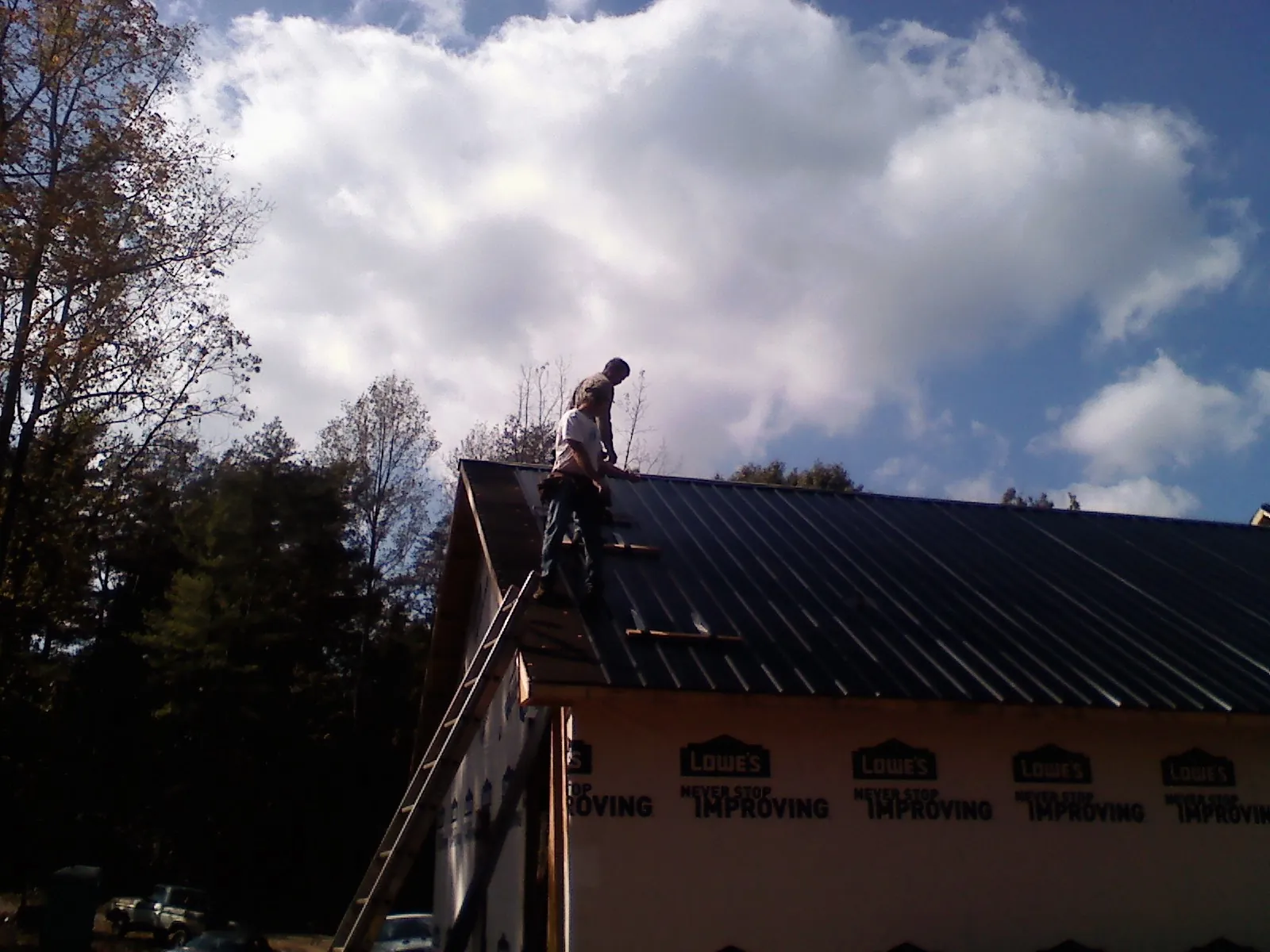 Roofer fastening dark metal panels high against a cloudy sky in Washingtonville