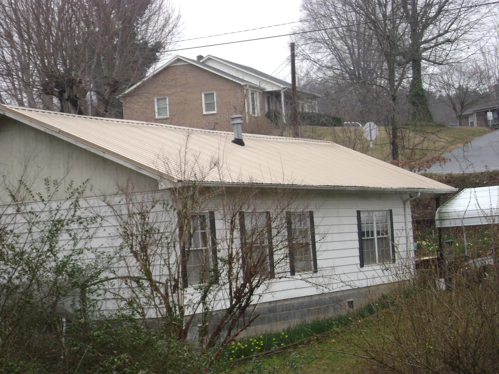 Tan metal roof on a white sided house set into a hillside — Commercial Roofing by Roofing Brothers in Washingtonville